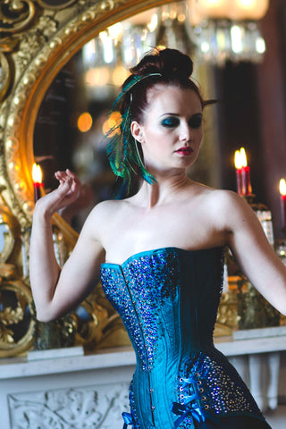 A fair red-haired model wears teal tights and a intricately beaded teal overbust corset