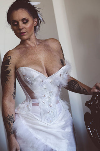 A fair model with freckles poses in a sheer and white panelled corset inspired by the Snowy Owl. The ensemble featured beadwork and feathers