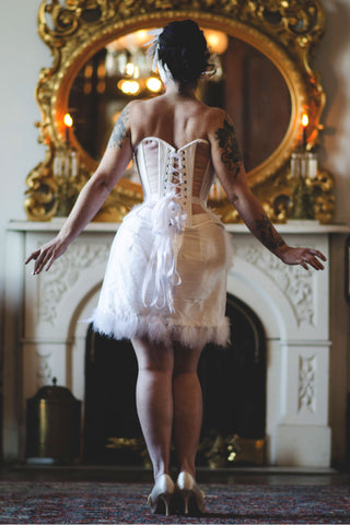 A fair model with freckles poses in a sheer and white panelled corset inspired by the Snowy Owl. The ensemble featured beadwork and feathers