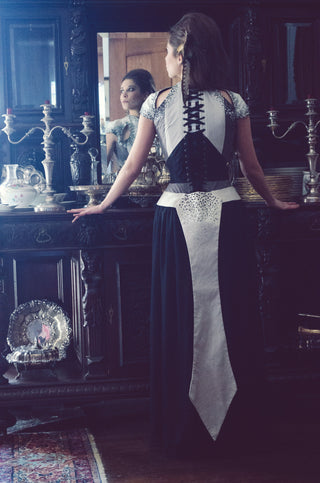 A brunette model wears a corset-ed ensemble that features grey and white panels, hand-beaded detailing and a long white tail reminiscent of a swallotail.