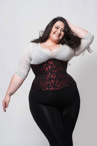 Red Rosebud Coutil black corset features delicate red floral detail. here it is worn by a plus sized brunette woman