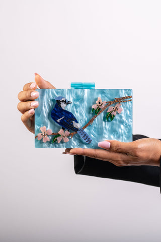 The Bad Button Kentucky blue jay purse sits in a white background, held by two hands