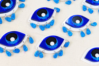 The Bad Button Apotropaic Eye earring sit all together on a white fabric background