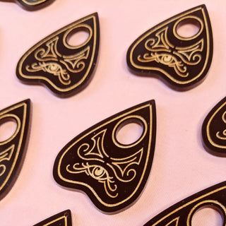 On a pink background sit black and gold ouija planchettes ready to be made into earrings