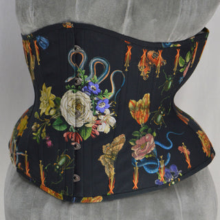 A Bad Button bespoke corset design by Alisha Martin featuring a black fabric covered in illustrations of flowers, snakes and insects
