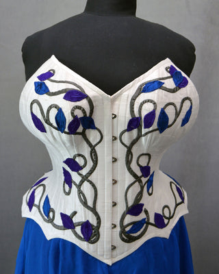 A Bad Button bespoke corset design by Alisha Martin featuring floral style embelishment on a white corset and matching blue skirt