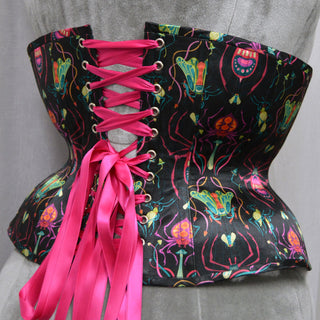 A Bad Button custom corset design by Alisha Martin featuring black fabric with brightly coloured insects and pink lacing
