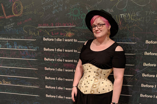 The Bad Button founder Alisha Martin stands against a chalk-graffiti wall. She wears a had, bold earrings and a custom corset in a bee fabric