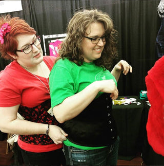 The Bad BUtton's founder Alisha Martin helps fit a woman in a corset an at expo.