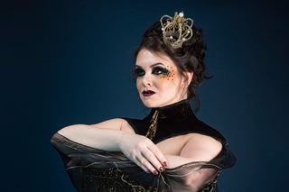 A fair skinned brunette plus sized model wears a handmade crown and bold black and yellow editorial makeup. She is wearing a bespoke corset design by The Bad Button that features hand beaded details and resembles a bee