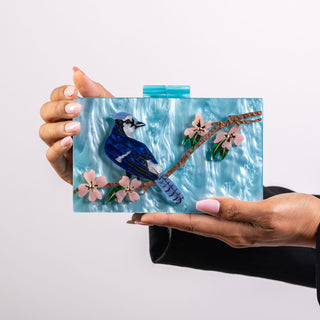 The Bad Button's beautiful acrylic purse is held by two hands. the bag is a light blue and features a design with a blue jay and pink flowers.
