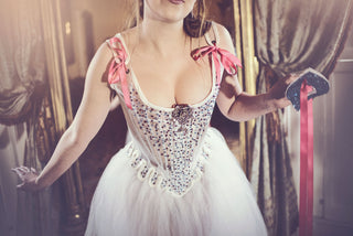Embellished white sheer set of stays and gown with pink lacing appear on a model with a glittery venetian-style mask