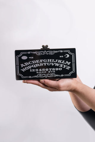 The Bad Button ouija spirit board purse with silver detailing is held by two hands