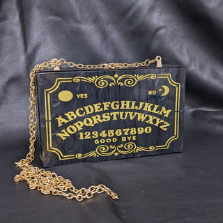 The Bad Button ouija board in gold sits in a grey background