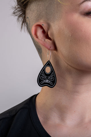 A woman with a shaved head wears the The Bad Button perfect planchette earrings in black