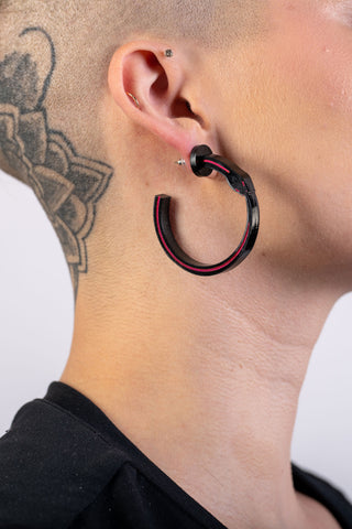 A woman with a shaved head wears the black and pink ourborus hoop earrings
