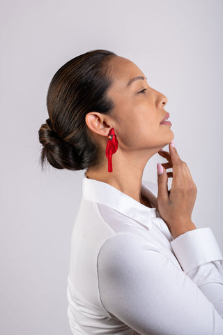 A woman in a white shirt wears the The Bad Button completely cardinal earings