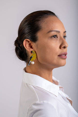 The Bad Button earrings featuring a yellow gold finch with pearl detailing are worn by a woman in a white shirt
