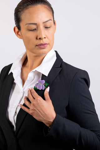 The Bad Button vibrant violet brooch is worn by a woman in a suit