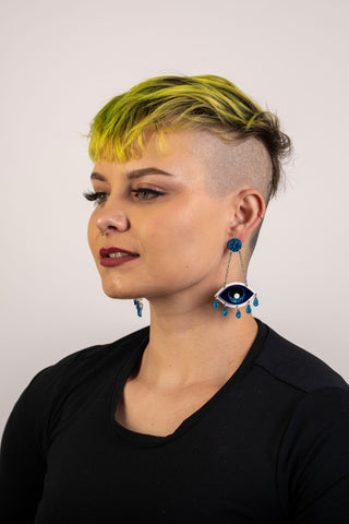 A woman with bright yellow hair wears the apotropaic eye dangle earrings